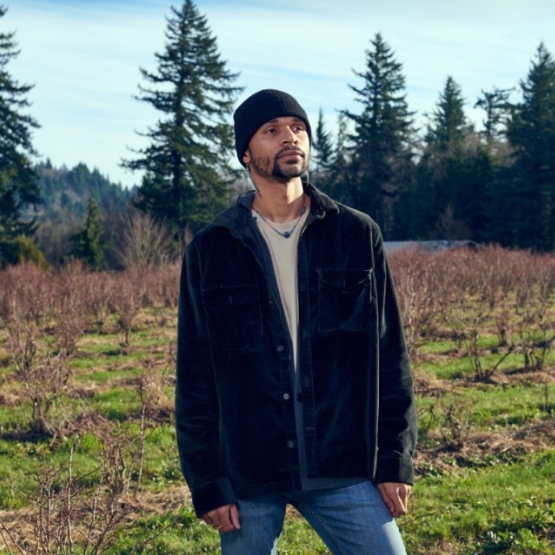 Christopher Rachal standing in a field with evergreens behind him